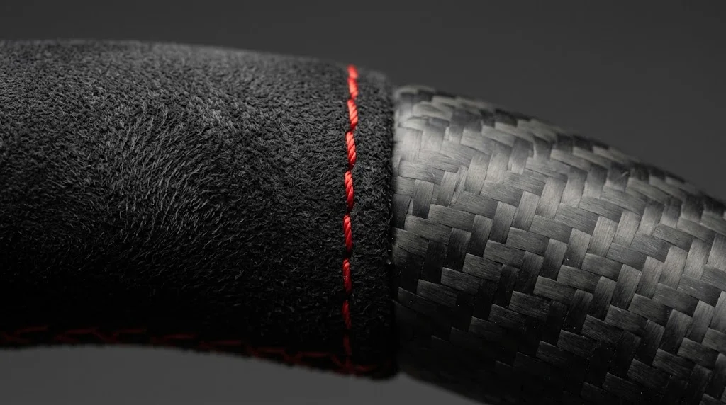 Close-up of black Alcantara, matte carbon fiber and guards red stitching on a CASSERON Porsche Boxster steering wheel