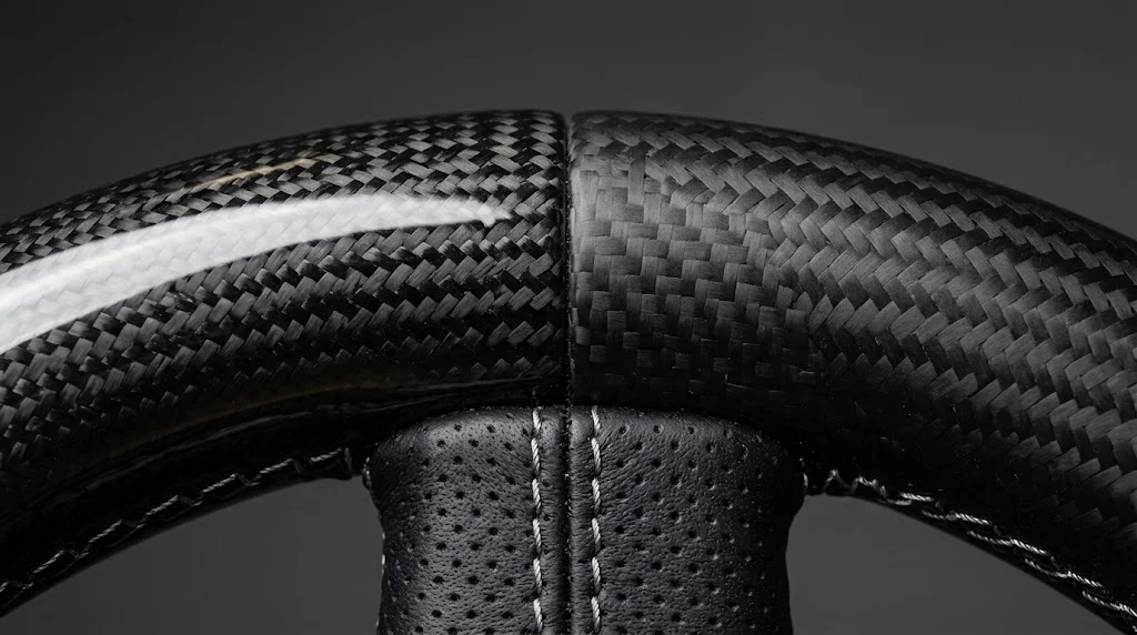 Close-up comparison of high-gloss carbon fiber and matte carbon fiber side by side on a CASSERON Porsche steering wheel rim with silver stitching