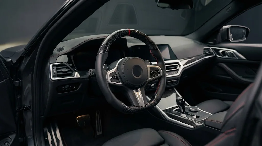 Interior view of a CASSERON custom steering wheel for Porsche Macan 95B and XAB, with forged carbon fiber trim, perforated black leather grips and racing yellow contrast stitching