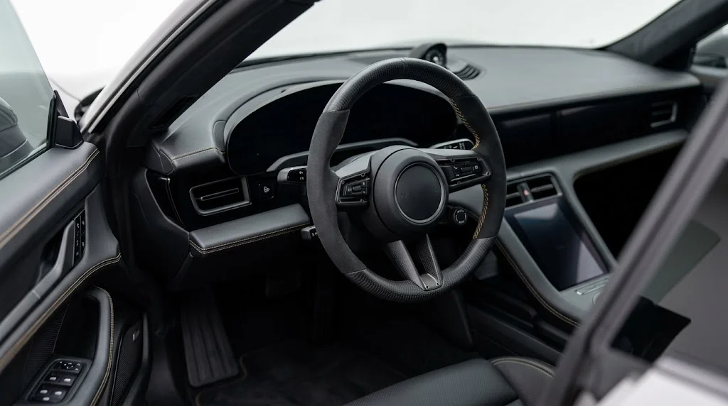 Interior view of a CASSERON custom steering wheel for Porsche Taycan Y1A and Y1B, with gloss carbon fiber trim, black Alcantara side grips and bronze contrast stitching